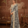 Woman wearing elegant off-white silk saree with black floral print and rich golden zari woven border, paired with matching blouse and traditional jewelry in a heritage-inspired setting.