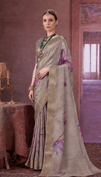 Elegant woman wearing a grey silk saree with golden zari border and purple floral prints, styled with traditional jewelry, standing in a royal vintage indoor setting.