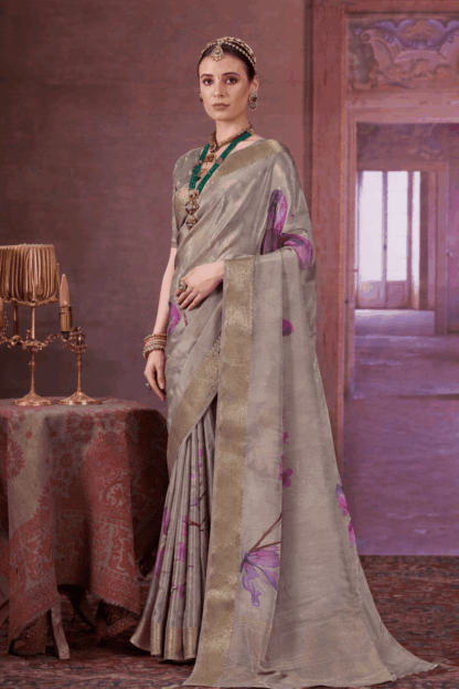 Elegant woman wearing a grey silk saree with golden zari border and purple floral prints, styled with traditional jewelry, standing in a royal vintage indoor setting.